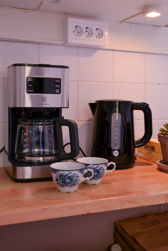 Kaffebryggare och tekorare med två blåmålade koppar framför, på köksbänken i det gemensamma köket.